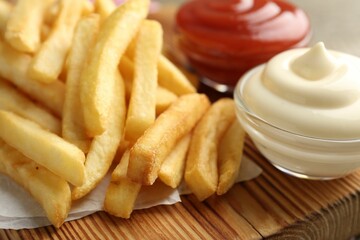 Tasty french fries with sauces on wooden table, closeup