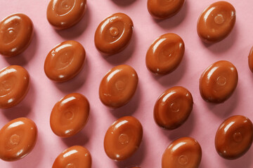 Many tasty caramel candies on light pink background, flat lay