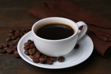 Aromatic coffee in cup, beans and saucer on wooden table, closeup