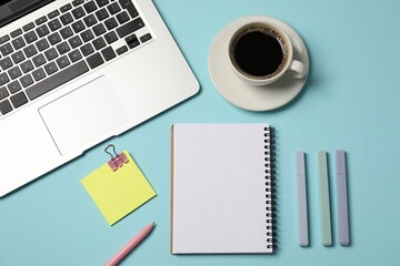 Notebook, other stationery, coffee and laptop on light blue background, flat lay