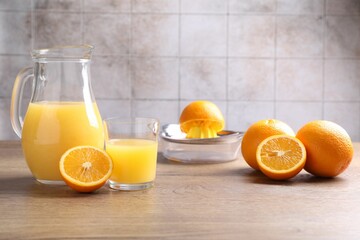 Fresh orange juice, fruits and squeezer on wooden table against grey tiled wall, closeup