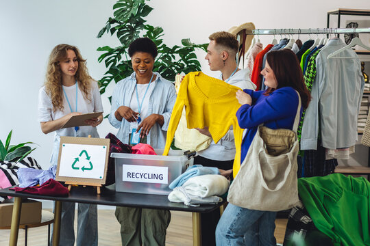 Concept of textile pollution, conscious consumption. Ecology, sustainable lifestyle. Group of volunteers, young women and man, sorting clothes in charitable foundation for charity donation, recycling