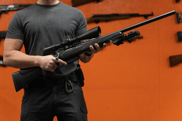 Man holds a high-precision rifle with an optical sight, preparing for training at a shooting range or indoor gallery.