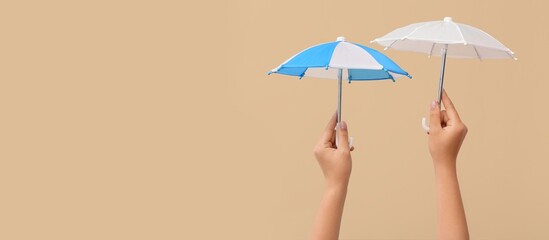 Hands holding small umbrellas on beige background with space for text