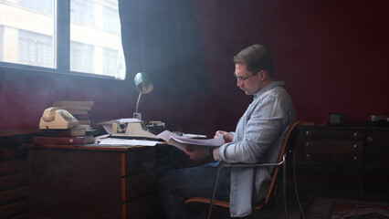 Soft-focused image of an author battling writer's block at his cluttered desk with laptop and...