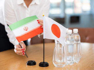 Little flag of Japan on table with bottles of water and flag of Iran put next to it by positive...