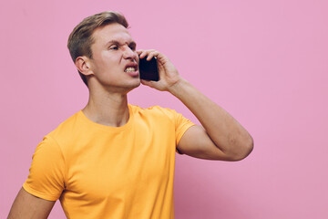 Man annoyed irritated talking on mobile phone wearing casual yellow t-shirt against pink...