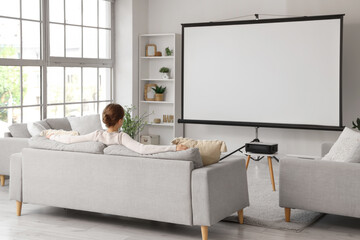 Woman sitting on sofa with projector screen in room, back view
