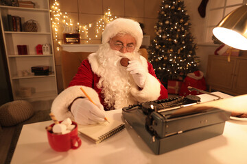 Santa Claus with typewriter and cookies taking notes while writing Christmas story at night