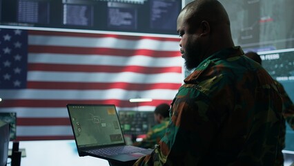 Intelligence officers in american military uniforms work on computers in a command post, managing...