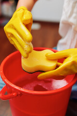 Woman in yellow rubber gloves washing a sponge in a bucket of water