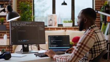 Male coder works from home typing code on a laptop in a modern living room. African american IT...