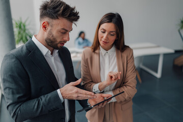 Business colleagues using digital tablet, discussing work in office