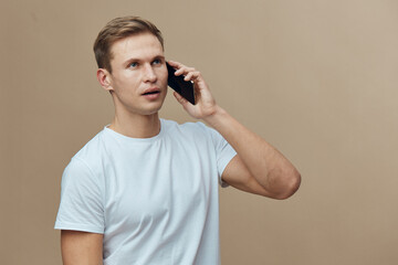 Fototapeta premium Young caucasian man talking mobile phone wear white t-shirt isolated on beige background digital nomad concept work remote technology communication portrait