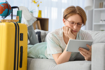 Male tourist with tablet computer booking hotel room online on sofa at home