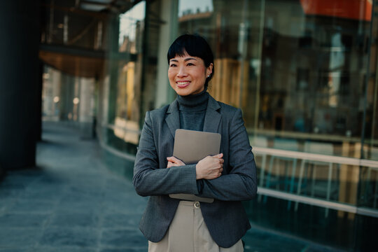 Smiling businesswoman holding laptop outside office building