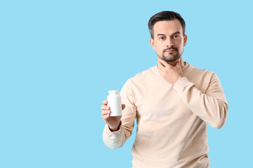 Handsome man with pill bottle self-examining thyroid gland on blue background