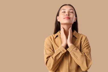 Young Asian woman self-examining thyroid gland on beige background
