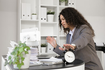 Stressed African-American businesswoman turning off alarm clock and trying to meet deadline in...