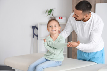 Fototapeta premium Cute little girl with physiotherapist stretching on couch in rehabilitation center