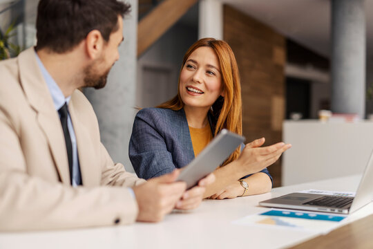 Smiling businesswoman sitting at boardroom and explaining business strategy to her coworker on sprint meeting.