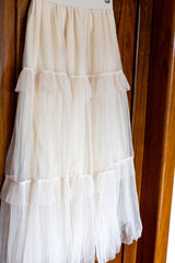White lace dress detail — elegant bridal skirt with delicate lace hem hanging on wooden background