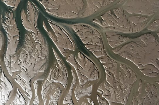 Abstract aerial top-down view of intricate tidal estuary patterns, showing the contrast between water channels and textured mudflats or marshes, natur