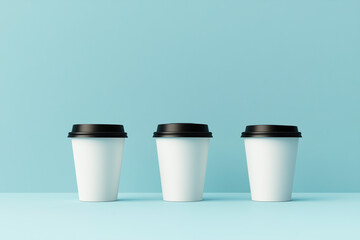 Three white takeaway coffee cups with black lids on a bright turquoise background.