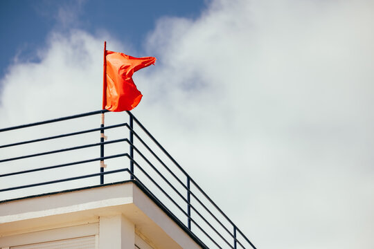 Red flag on rooftop railing against cloudy sky