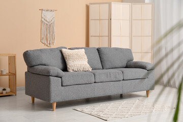 Interior of stylish living room with comfortable sofa, shelving unit and dressing screen near beige wall