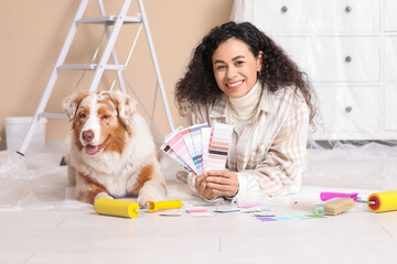 Happy female African-American painter with palette samples and cute Australian Shepherd dog lying...