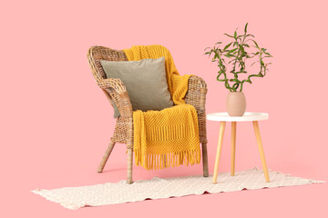 Table with bamboo stems in vase, wicker armchair and rug on pink background