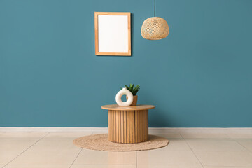 Stylish coffee table with rug, chandelier and photo frame near dark turquoise wall