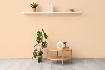 Stylish coffee table with houseplants, shelf and decor near beige wall