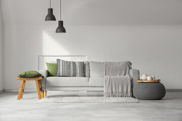 Interior of light living room with grey sofa, pouf and table