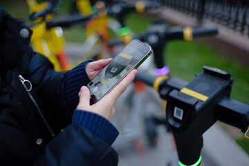 Scanning by smartphone QR code of kicksharing system electric scooters on city street at daytime. Shallow depth of field