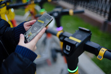 Scanning by smartphone QR code of kicksharing system electric scooters on city street at daytime. Shallow depth of field