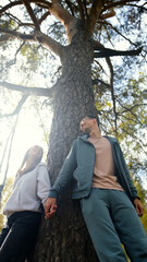 Fototapeta premium Lovers boy and girl standing near a big pine tree during a walk on a sunny autumn day