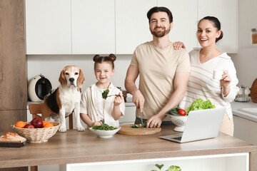 Cute little girl with her parents and Beagle dog cooking vegetable salad in kitchen