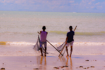 Selective focus on fishermen pulling a fishing net on the shore of a sandy beach. The background and foreground are blurred, highlighting the action and teamwork.