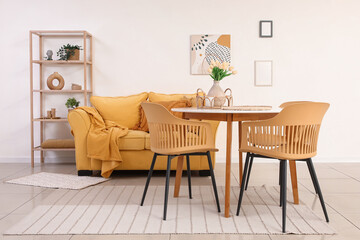 Interior of light room with dining table, yellow sofa and shelf unit