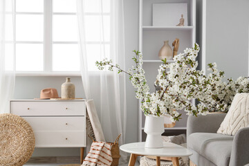 Vase with flowering branches on table in light living room