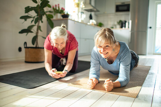 Senior lesbian couple motivating each other while exercising and working out at home and using a stopwatch on their smart phone to time each other