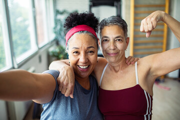 Happy senior women taking selfie after workout at gym flexing muscles