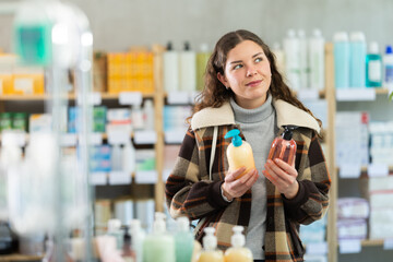 Female buyer chooses liquid hand soap in household goods department of the supermarket