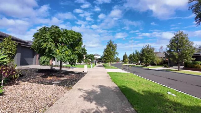 A clean and peaceful suburban street in Melbourne Australia's outer suburb showcasing established trees, manicured lawns on nature strips, concrete footpaths, and contemporary homes.