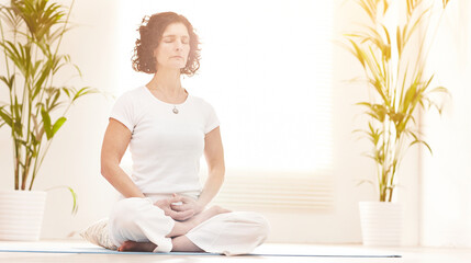 Mature woman meditating in a yoga studio or at home. Active female practicing breathing techniques...
