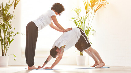 Female yoga instructor training a man to do downward dog pose during a fitness class in an exercise...