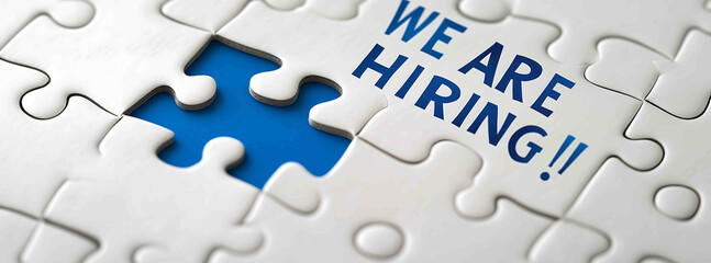 A white puzzle with one blue piece with the text WE ARE HIRING on the white background The concept of team building and adding new team members to your company or looking for them i