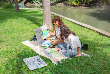 Mother and daughter designing impactful environmental posters by the river